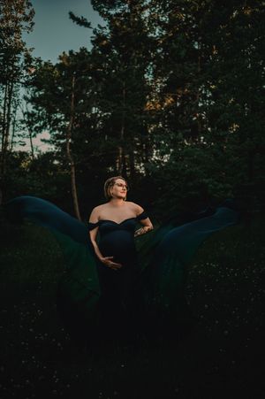Artistic outdoor maternity silhouette against a dusky blue sky with trees in the background.