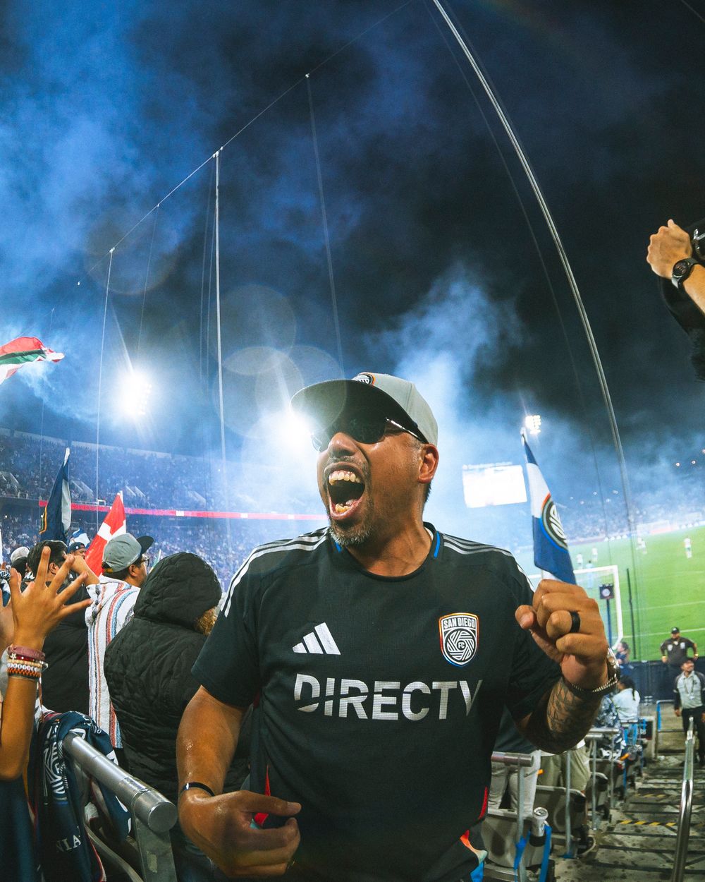 a fan celebrates with blue smoke and bright lights in the background