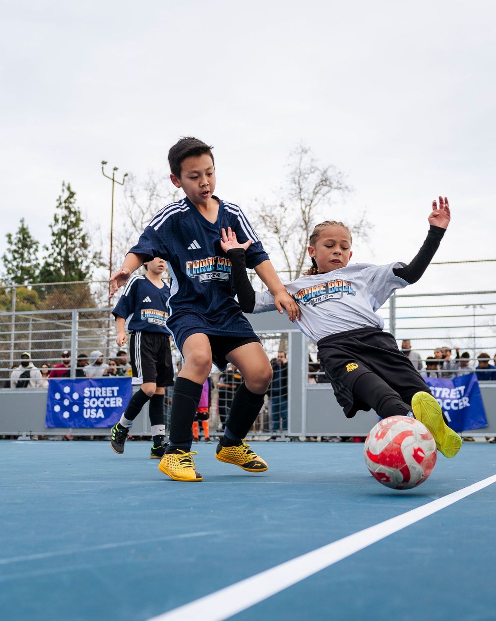 Two young soccer players fight for a ball, one slides to keep the ball in bounds