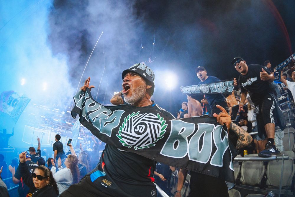 A fan cheers passionately with blue smoke rising in the background