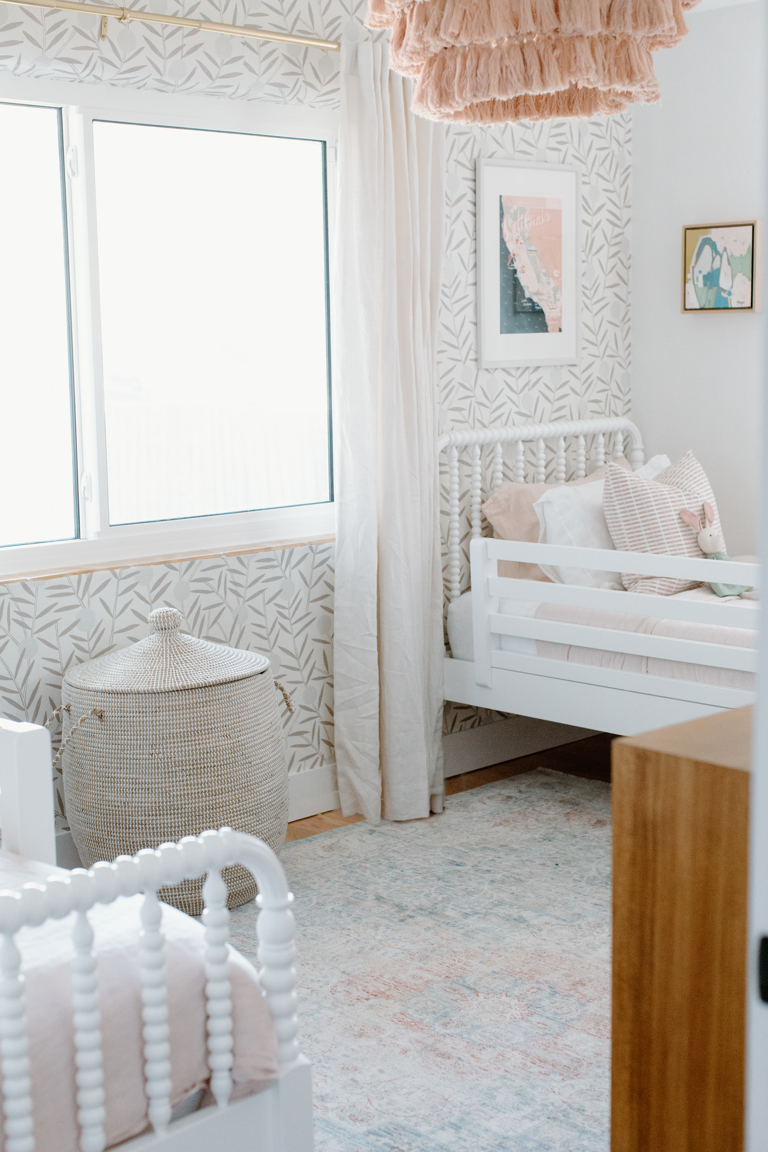 Modern nursery room with white spindle bed, pink accents and geometric pattern wallpaper.