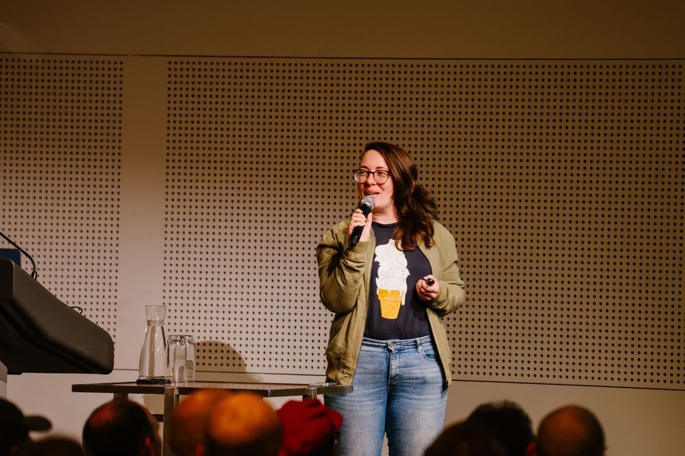 A performer holds a microphone and gesture animatedly on stage during a live show or presentation.