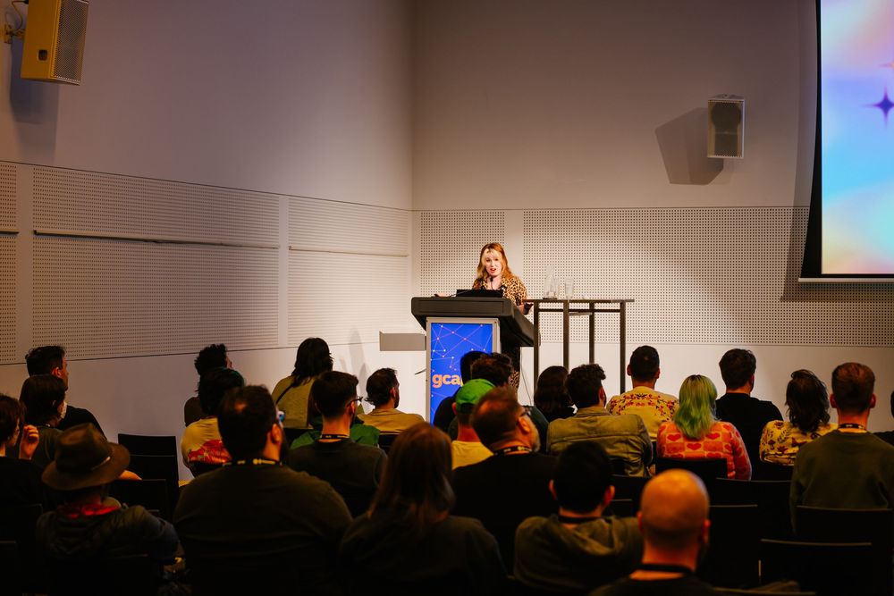 A dark silhouette of conference attendees watching a presentation screen in a dimly lit meeting room.