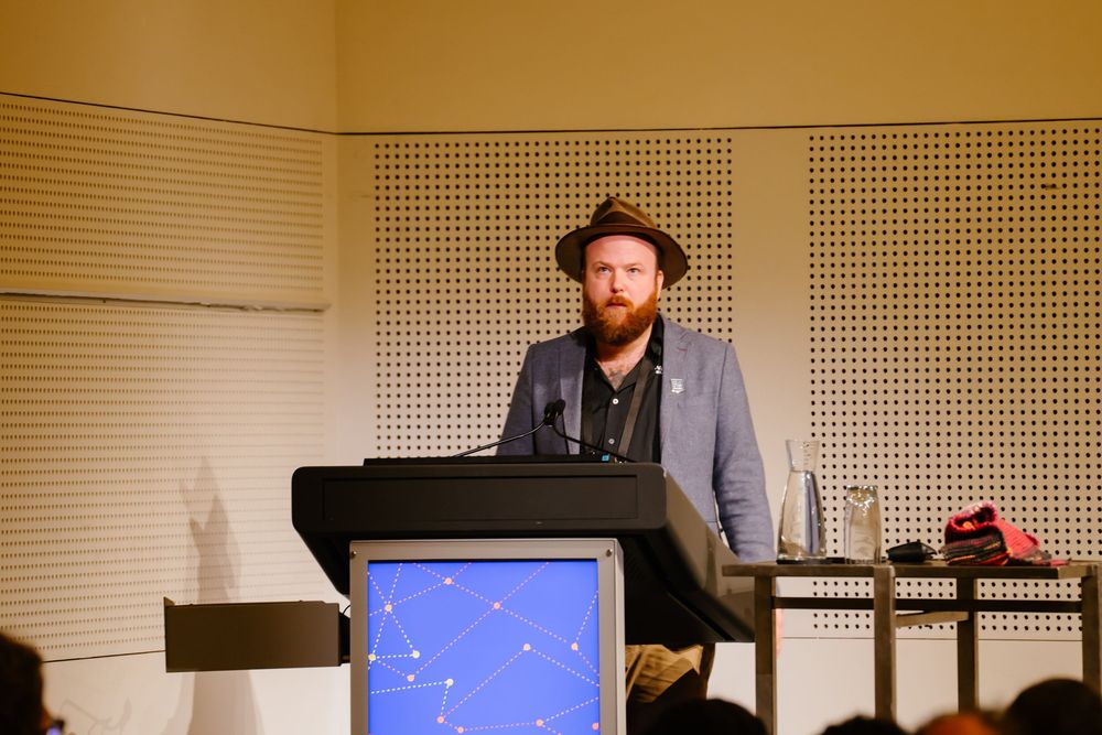 Musicians perform in a studio setting with acoustic panels visible on the walls and digital displays in view.