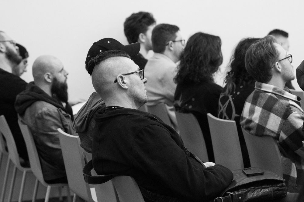 A black and white photo of people sitting in a row of chairs at an event or meeting.