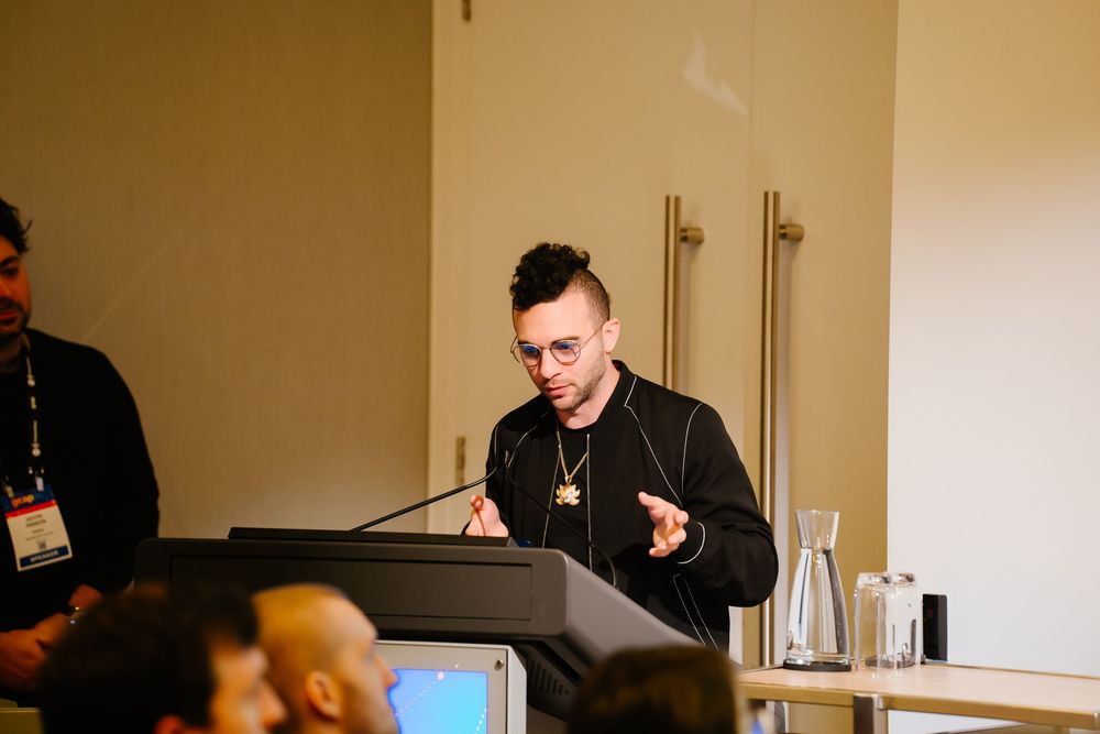 Someone speaks at a podium during what appears to be a conference presentation with a water bottle visible.