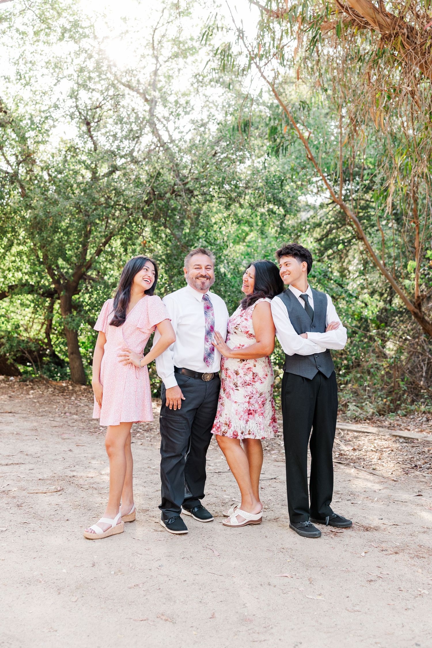 Four people in formal attire pose together outdoors, with lush greenery in the background.