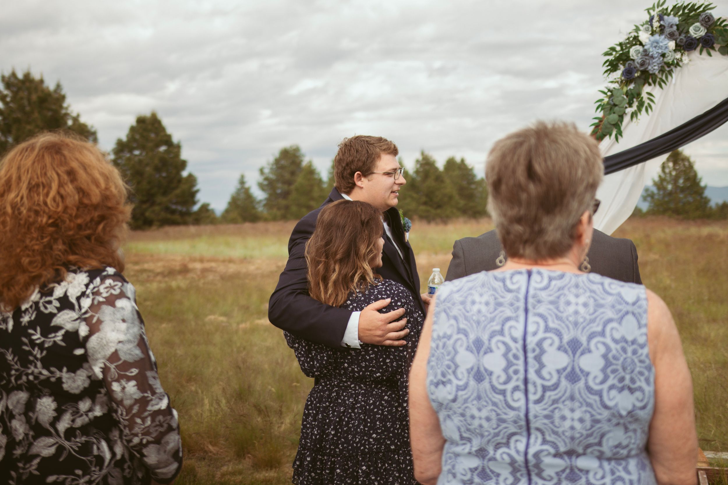 A couple stands in a golden grassy field during an outdoor photo session at sunset.
