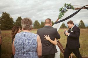 Wedding guests gather outdoors in a field with cloudy skies during an intimate outdoor ceremony.