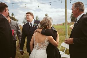 Guests gather at an outdoor wedding reception under strung lights during golden hour.