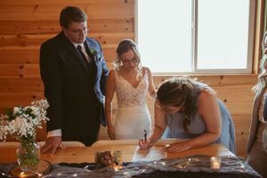Marriage paperwork being signed at a rustic wooden cabin during wedding ceremony with vase of white flowers on table.