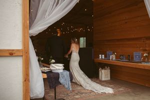 A wedding dress with a flowing train hangs gracefully in a rustic wooden room decorated with twinkle lights.