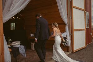 Bride and groom illuminated by sunlight share their first dance on a wooden floor in a rustic venue.