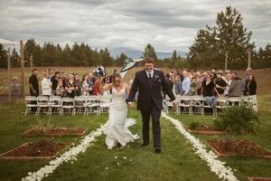 A couple celebrates while walking down a petal-lined aisle at an outdoor wedding with mountain views.