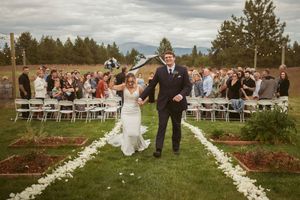 Joyful couple walks down a white petal aisle during their outdoor wedding ceremony.