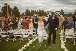 Newlyweds exit their outdoor ceremony along a flower-lined aisle while guests celebrate.
