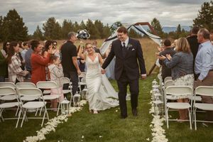 Outdoor wedding ceremony setup with white folding chairs and white flower petals lining a grassy aisle.