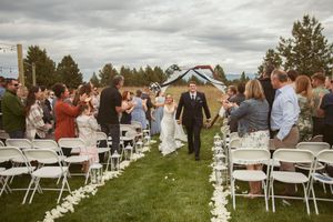 A scenic outdoor wedding ceremony setup with white chairs and mountain views under overcast skies.