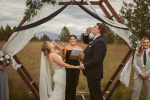 Wedding ceremony takes place under a wooden hexagonal arch decorated with white fabric in an outdoor rural setting.