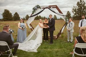Rustic outdoor wedding ceremony with geometric wooden arch and white draping in mountain landscape setting.
