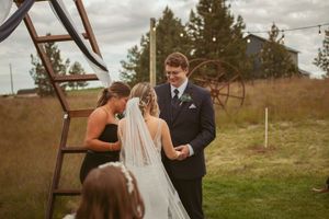 An intimate wedding ceremony under a rustic wooden arch in a mountain setting.