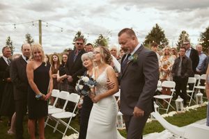 An outdoor wedding ceremony with guests seated on white chairs and mountains in the background.