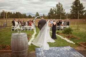 Outdoor wedding ceremony setup with wine barrel decor and white chairs on grass with mountain backdrop.