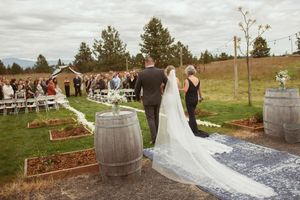 An outdoor wedding ceremony setup features wine barrels and white chairs on a grassy hill with mountain views.