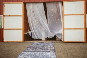 A decorated barn entrance with flowing white curtains and a grey runner leading to wooden doors.