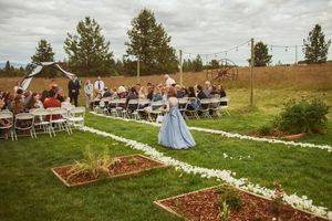 Outdoor wedding venue with white flower petals lining aisle and wooden garden boxes on rustic grounds.