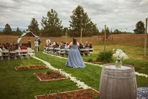 A rustic outdoor wedding venue with white petal aisle markers, wine barrels, and wooden garden boxes.