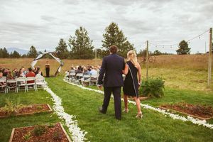 Couple walks down petal-lined aisle at rustic outdoor wedding ceremony with farmland backdrop.