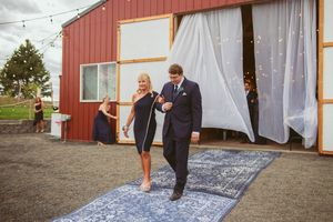 A joyful exit from a rustic barn venue onto a decorative grey runner during a wedding celebration.