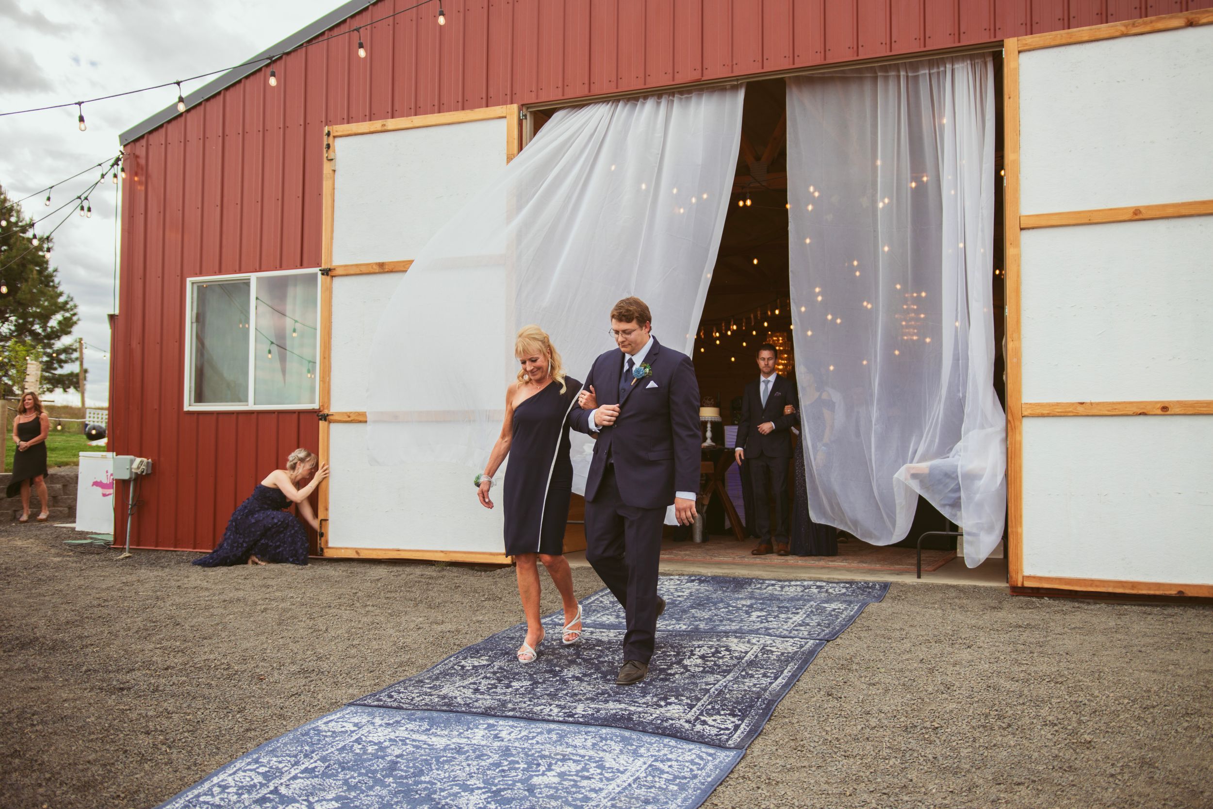 A rustic barn entrance decorated with white fabric draping creates an elegant outdoor wedding ceremony backdrop.