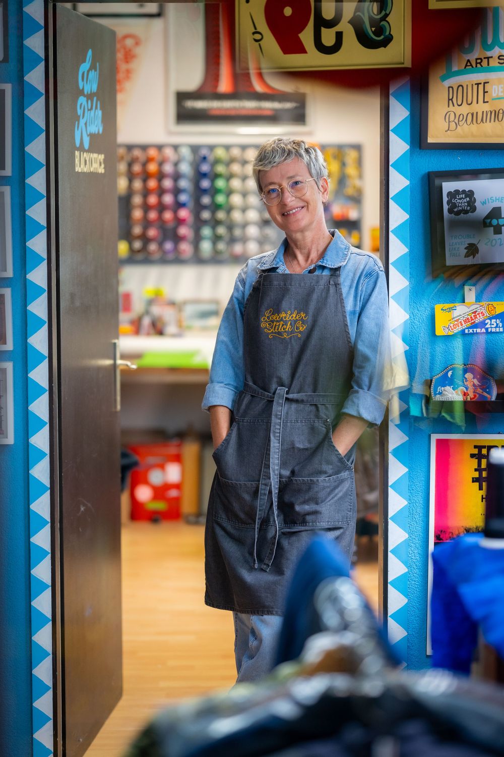 Person wearing denim work clothes and smiling in a colorful retail store environment.