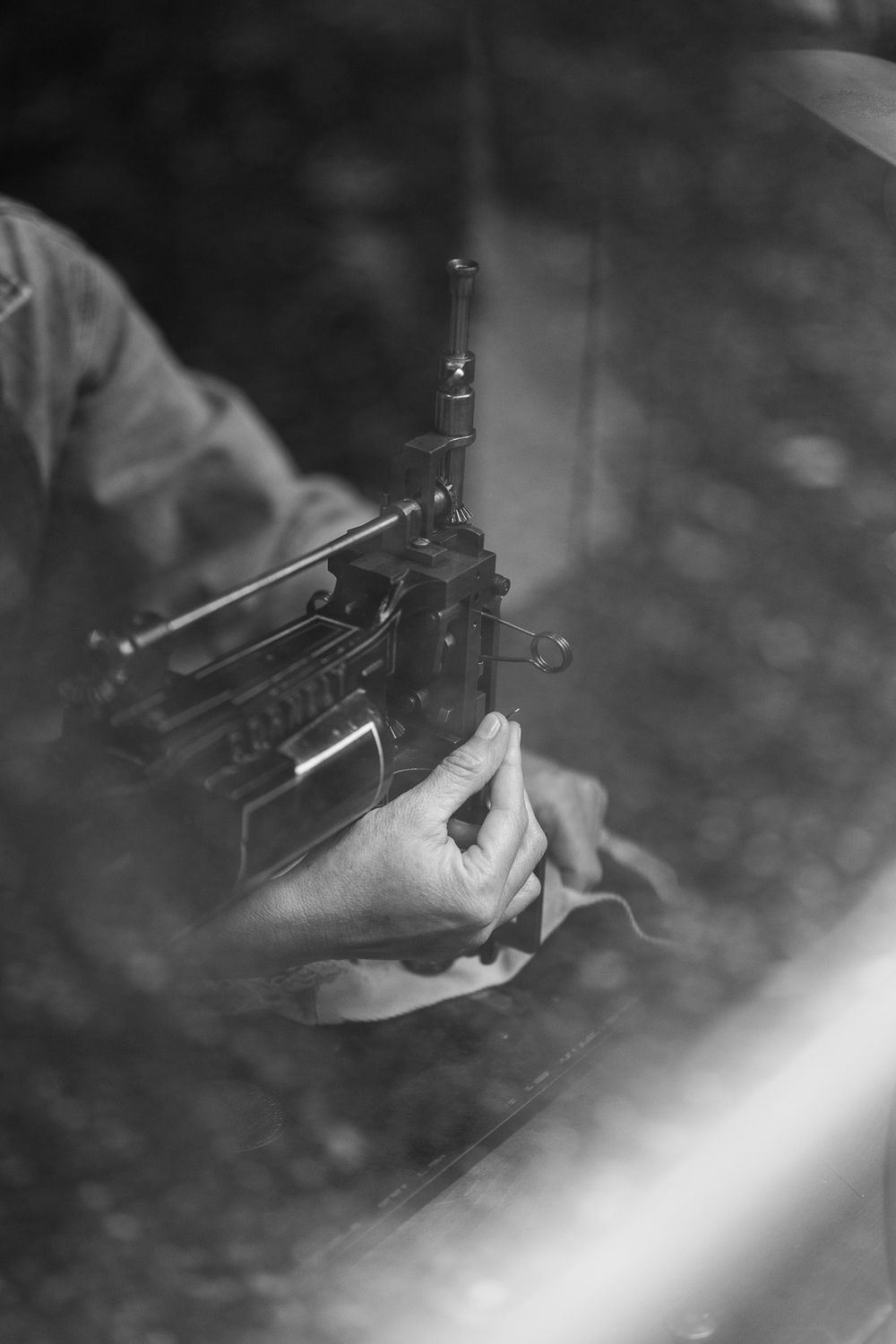 Black and white close-up shot of hands holding a gun mechanism or weapon part with blurred background.