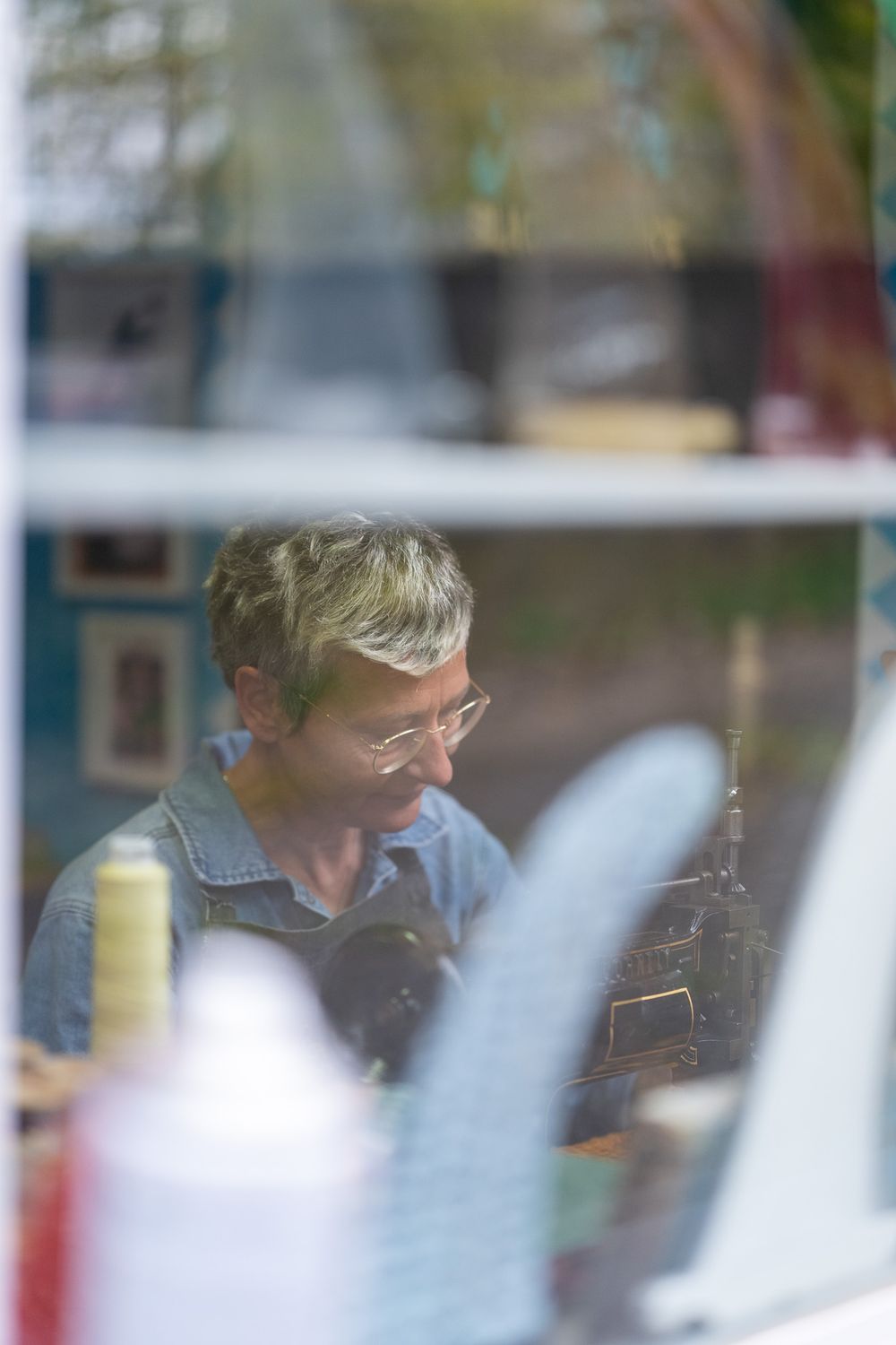 Through a window reflection, a person wearing glasses and denim is seen in soft focus lighting.