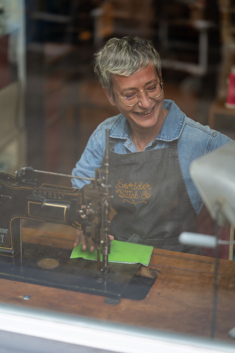 A seamstress at work behind a vintage sewing machine in a workshop setting.