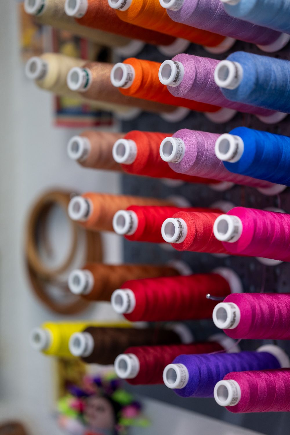 Rows of colorful sewing thread spools in pink, purple, blue, yellow and red arranged on display racks.