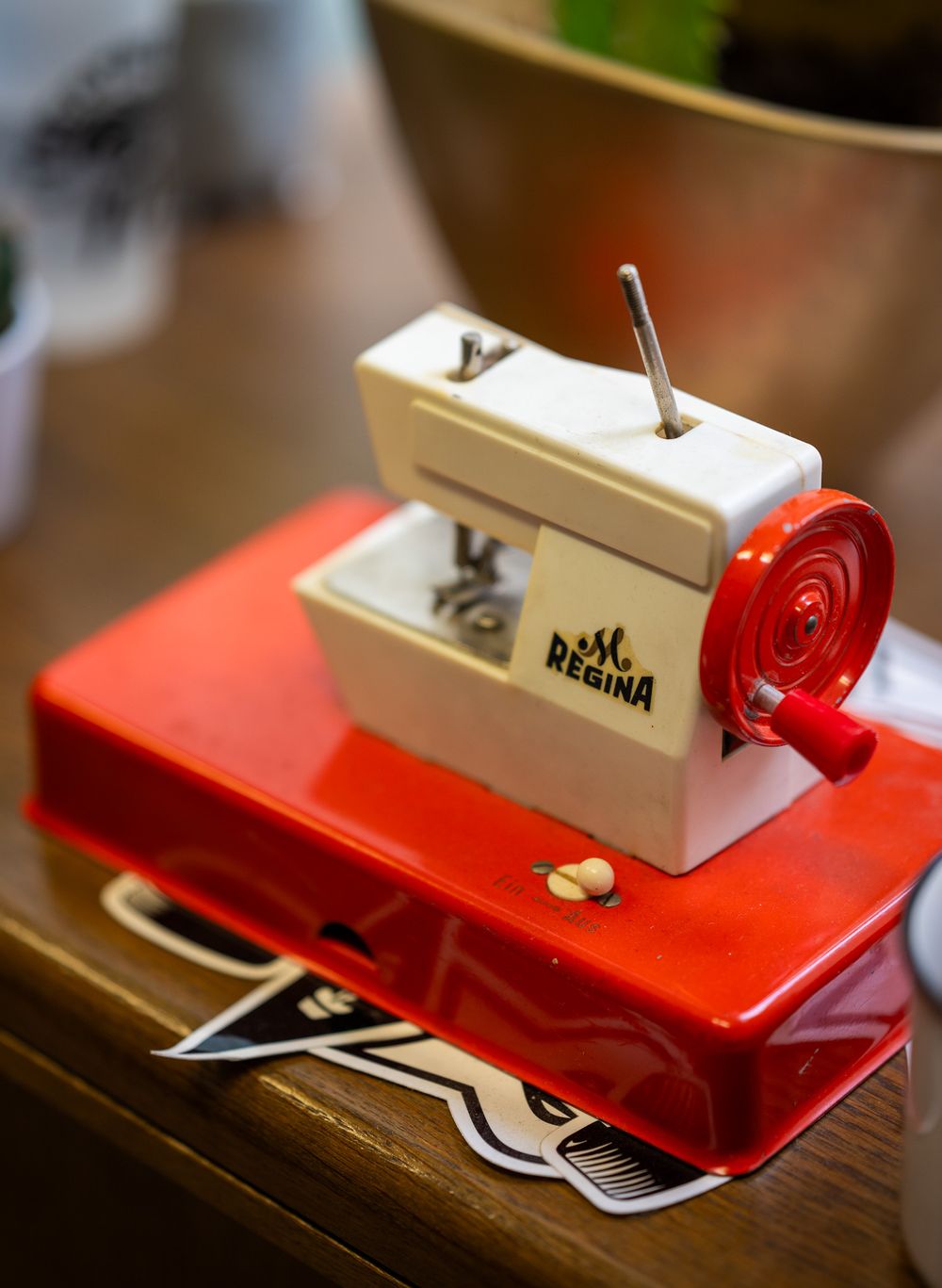 A vintage red and beige Regina toy sewing machine with a circular red attachment sits on a wooden surface.