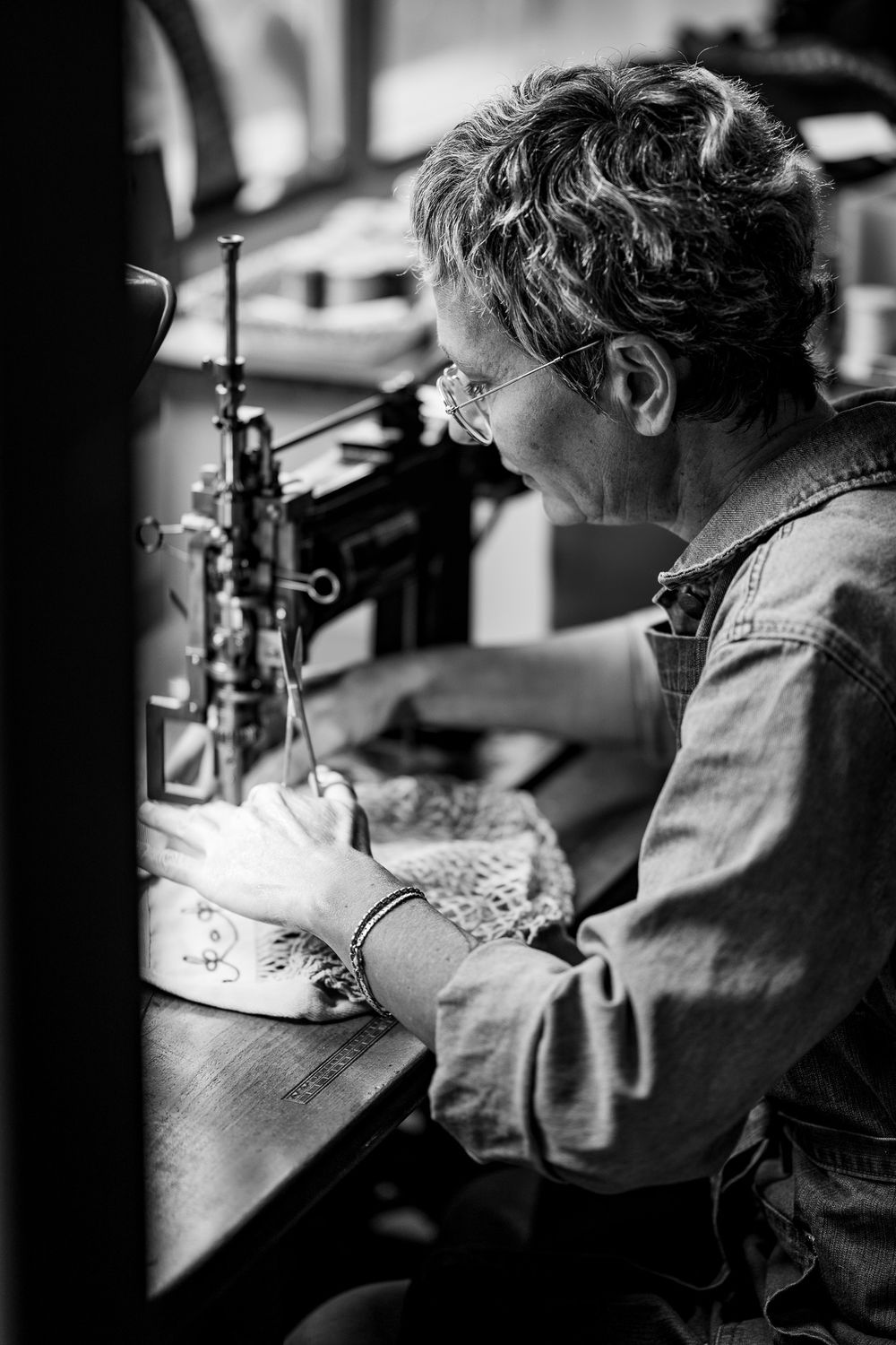 Black and white photo sequence of a person examining a garment using an industrial sewing machine in a workshop.