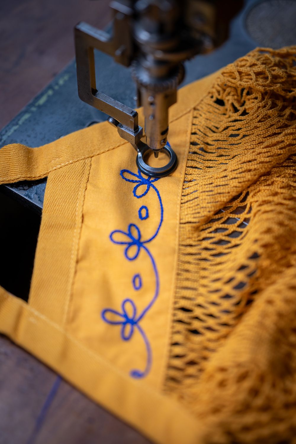 Close-up sequence showing blue decorative stitching being sewn onto golden fabric using a sewing machine.