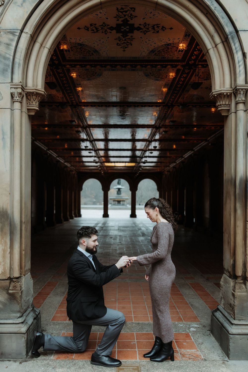 A romantic proposal moment in an ornate archway corridor with terracotta tiles and dramatic lighting.