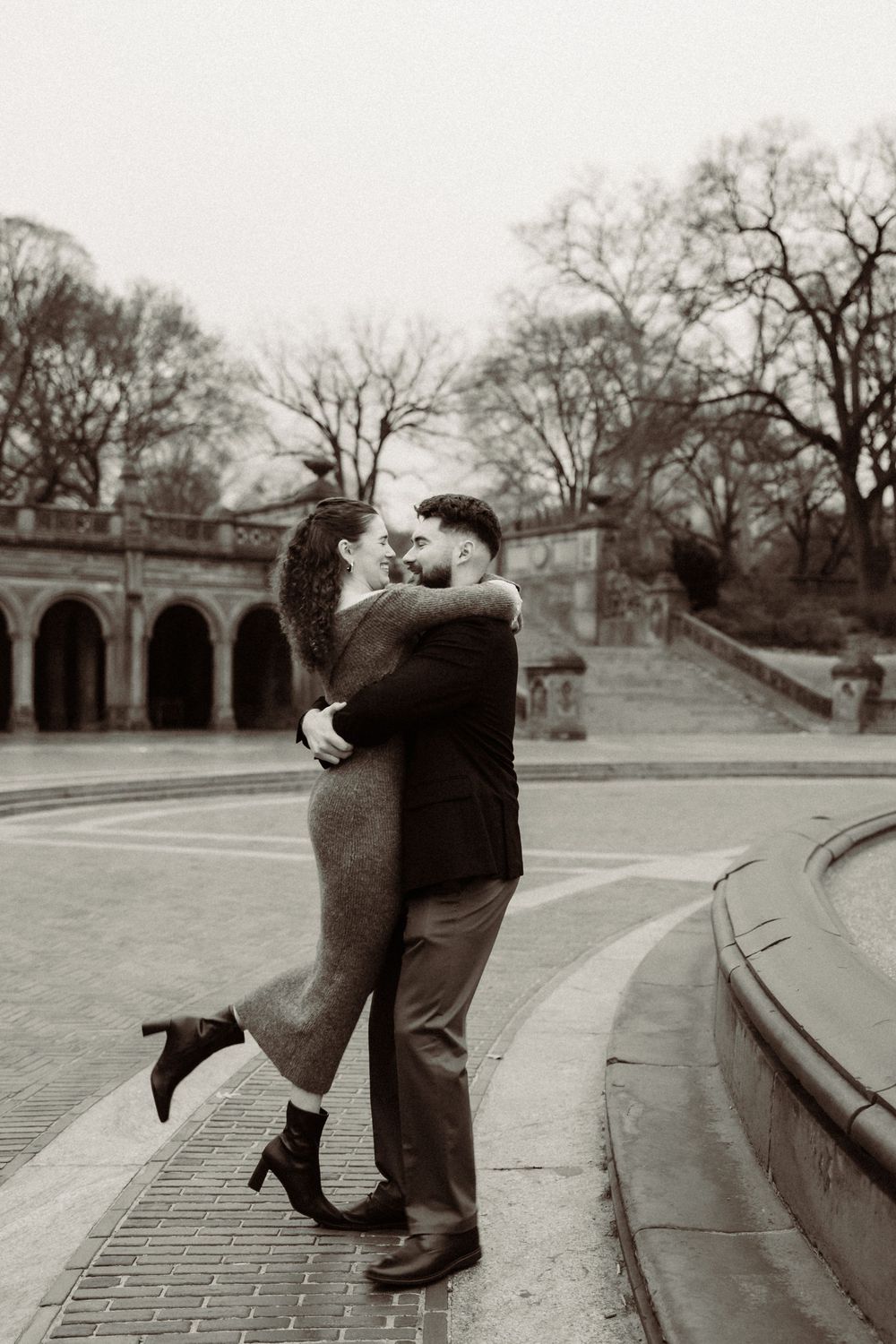 Vintage black and white photograph of a romantic embrace at Central Park's Bethesda Terrace with stone arches in background.