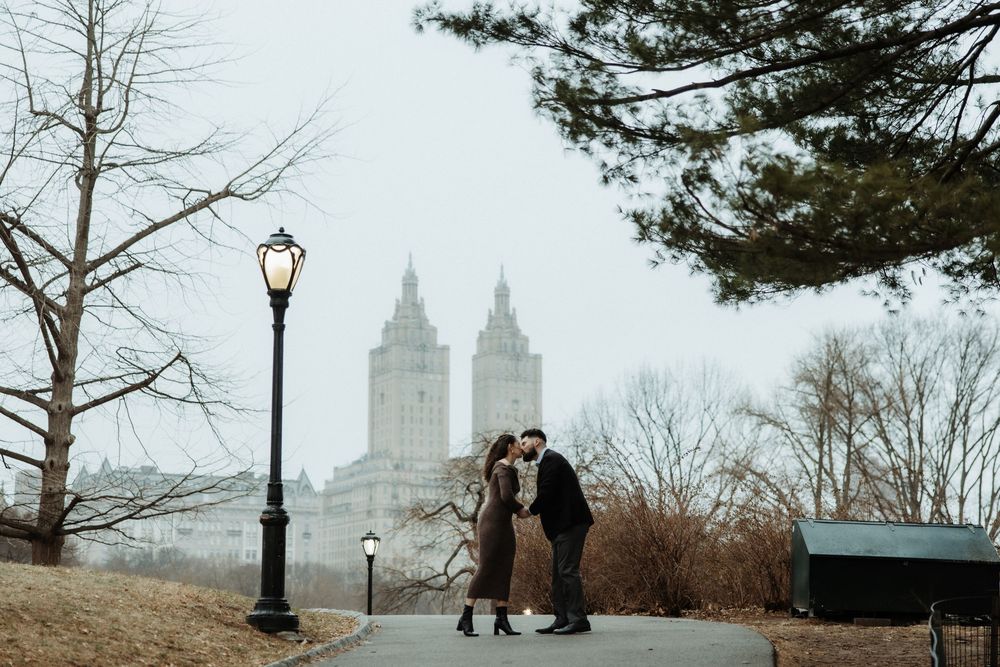 A couple shares an intimate moment on a foggy winter day in Central Park with the iconic El Dorado building in the background.