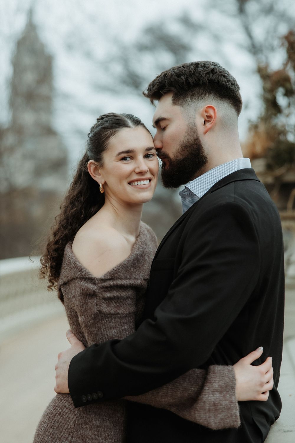 A romantic outdoor portrait of a couple embracing with a soft autumn background and blurred architecture.