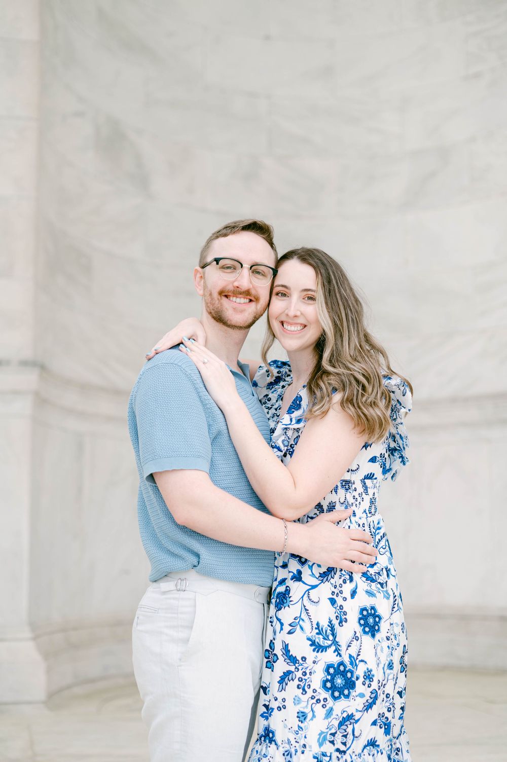 A romantic portrait against a white marble wall showcasing coordinated blue and white outfits.