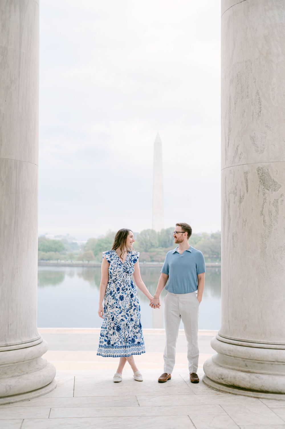 A couple poses between marble columns with the Washington Monument visible in the background.