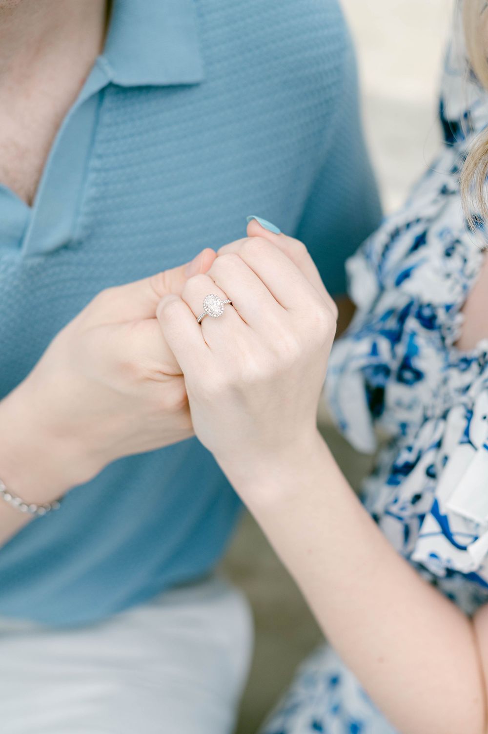 Close-up of hands showing off an engagement ring against blue and floral clothing.