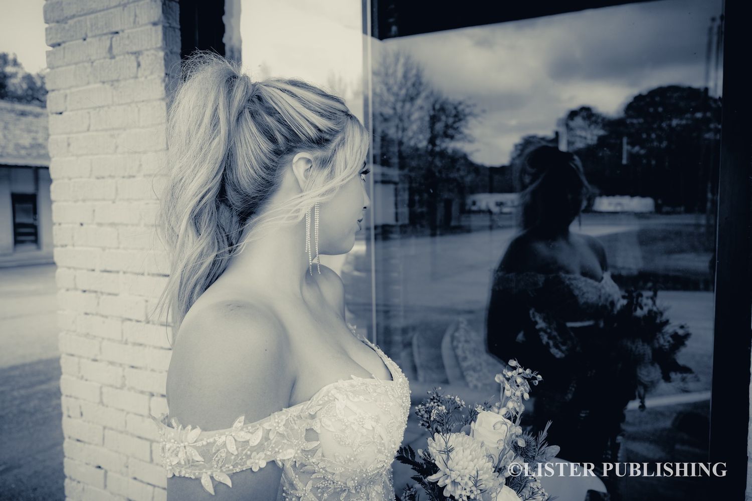 A dreamy black and white photo of a bride in a lace dress gazing through a window with a reflection visible.